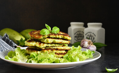Zucchini pancakes with sauce and garlic on a concrete black background.
