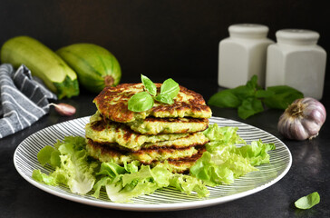 Zucchini pancakes with sauce and garlic on a concrete black background.