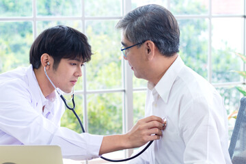 Fototapeta premium Handsome young doctor examines a middle-aged male patient with a stethoscope in a hospital office.