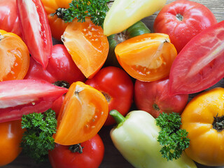 Red and yellow tomatoes of various varieties, sweet peppers, curly parsley on a wooden table close-up. Fresh seasonal vegetables, top view. Gardening and farming