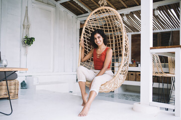 Happy woman resting in hanging chair at home