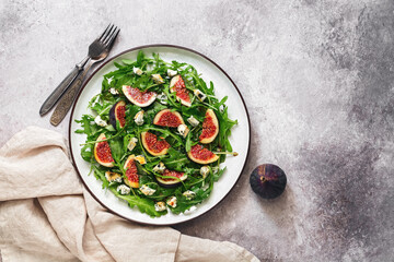 Fresh diet salad figs, arugula and blue cheese in a plate on a rustic beige background. Vegan and vegetarian lunch or dinner. Top view, flat lay, copy space.