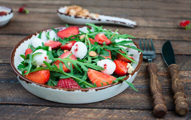 Salad with fresh strawberries, arugula, and mozzarella with nuts on rustic wooden background side view.