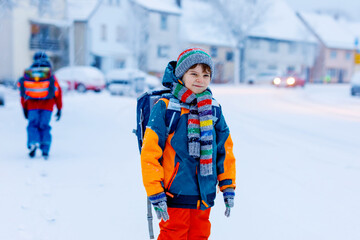 Two little kids boys of elementary class walking to school during snowfall