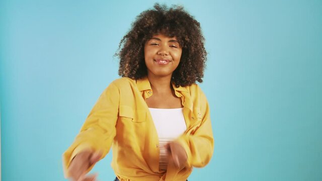 Young afro american female is smiling and pointing at you by forefingers while posing against blue background