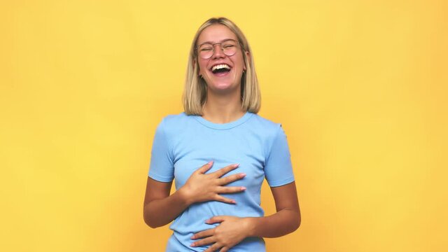 Young blonde caucasian woman laughs happily and has fun keeping hands on stomach
