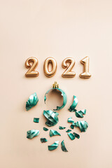 Gold numbers 2021 next to a broken Christmas tree toy on a pink background.
