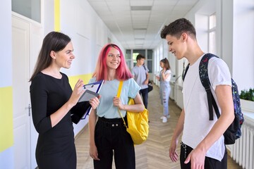 Group of teenage students talking to a female teacher in school corridor