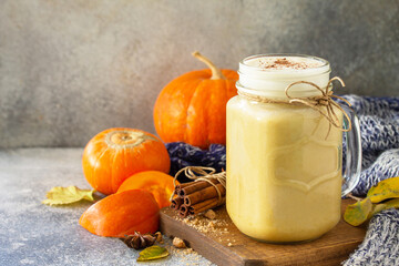 Autumn pumpkin spiced latte or coffee in glass with organic ingredients on a light stone countertop.