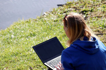 Girl sitting with a laptop in a autumn park on lake coast. Concept of student, freelance, remote work outdoor