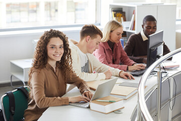 Portrait of smiling young woman looking at camera and smiling while studying with group of students...