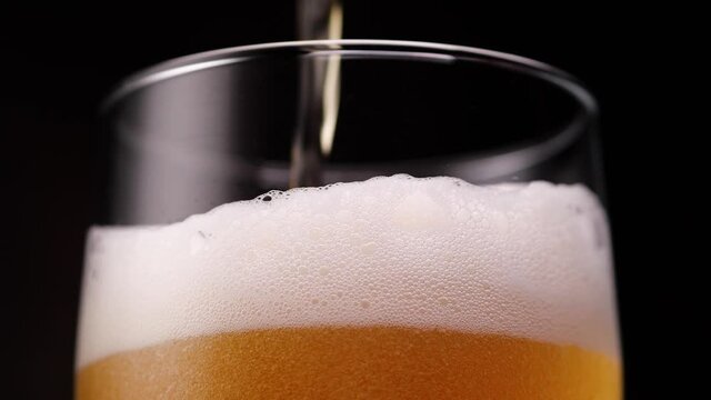 Low angle of trickle of fresh foamy beer pouring into glass cup on black background