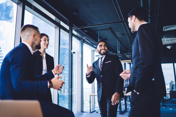 Happy multiracial male and female partners laughing during working day in corporate company, cheerful diversity group of employees enjoying brainstorming meeting for collaborating in office interior