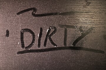 Thick layer of dust on a shelf with word dirty written in it