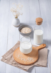 a glass of vegan  oatmeal milk on a cutting board with oatmeal flakes on a white wooden background