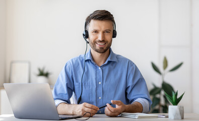Portrait of smiling male customer service operator in headset at workplace - obrazy, fototapety, plakaty