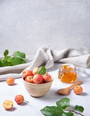 several juicy mini apples in a wooden bowl and a jar of jam on a light background.