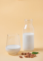 a glass and bottle of  almond milk and a few scattered nuts on a yellow  background