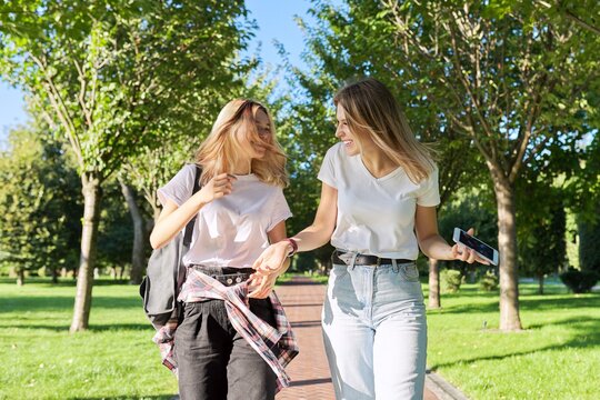 Two beautiful happy girls teenagers 17, 18 years old walking together in park