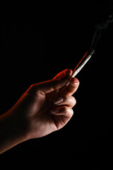 Woman hand holding cigarette in a smoke against black background. Smoking cannabis joint. Medical use.