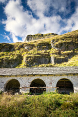 Obraz premium Mountain landscape, blue sky and white clouds, green slopes. In the foreground, an ancient stable. Piani Eterni, Dolomiti Bellunesi National Park, Italy