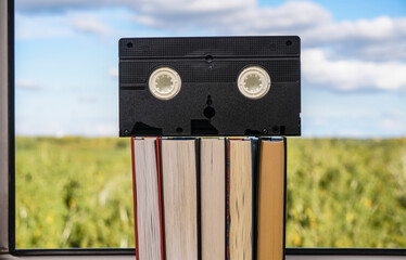VHS cassette on stack of books. blue sky background. Window frame.