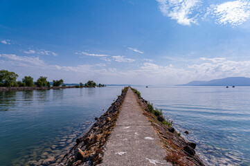  View on a very long dike leading to the Tene lighthouse on Lake Neuchatel in Switzerland. The blue sky is reflected in the calm water of the lake.