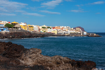 Fototapeta na wymiar Black volcanic rocks framing the traditional Spanish village with colorful buildings, a small harbor and the Atlantic ocean in front, in Los Abrigos, Tenerife, Canary Islands, Spain
