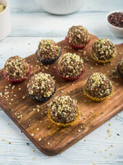 Home made vegan energy protein balls with oats, nuts, dates, dried fruit, flax and hemp seeds, chocolate nibs and maple syrup served in paper cases on wooden board. Vertical