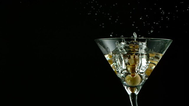 Super Slow motion shot of olives splashing into Dry Martini Drink
