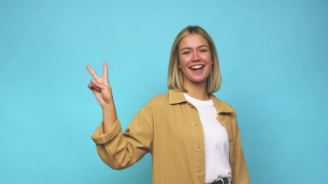 Young blonde caucasian woman joyful and carefree showing a peace symbol with fingers