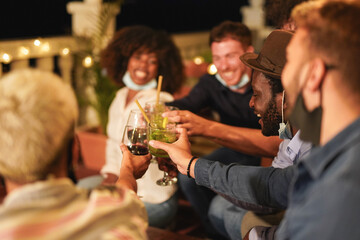 Happy multiracial people cheering with drinks while wearing surgical face mask under chin - Concept of private party at home because of coronavirus