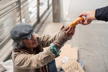 Aged homeless beggar reach out to get bread on donor hand at the bridge