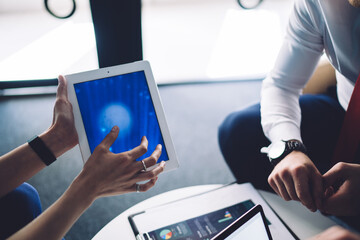 Crop anonymous woman with tablet showing online program to coworkers in office