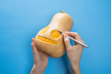 Woman hold carved pumpkin jack craft knife tool in hand  halloween holiday on a blue background	
