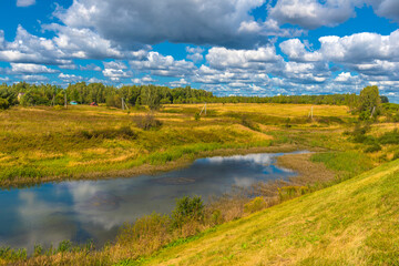 yellow field and blue sky with clouds and lake