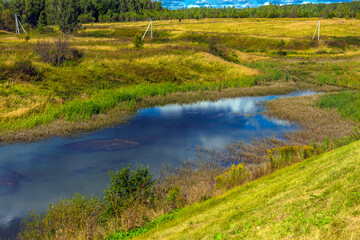 yellow field and blue sky with clouds and lake