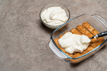 tiramisu dessert cooking - Traditional Italian Savoiardi ladyfingers Biscuits and cream in glass baking dish on concrete background