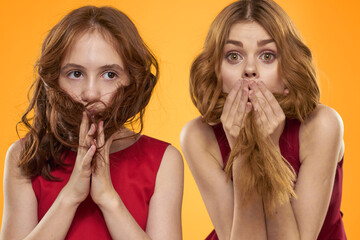 A red-haired girl and a beautiful woman on a yellow background in red dresses gesticulate with...