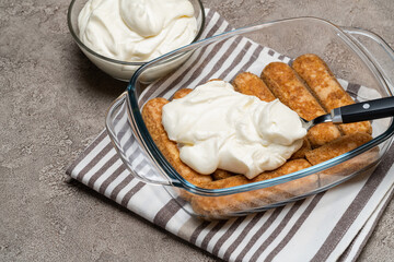 tiramisu dessert cooking - Traditional Italian Savoiardi ladyfingers Biscuits and cream in glass baking dish on concrete background