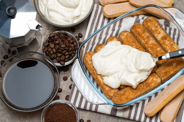tiramisu dessert cooking - Traditional Italian Savoiardi ladyfingers Biscuits and cream in glass baking dish, coffe maker on concrete background