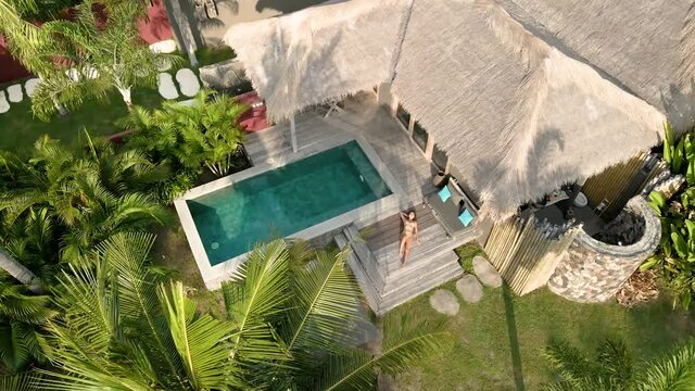 Girl enjoying good weather in luxury villa hotel with private pool surrounded by palm trees.Aerial flyover.