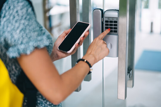 Cropped image of woman entering building using security code and connection on mobile phone for passing, female pressing buttons entering secret key code for unlocking doors and home system