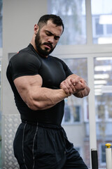 Naklejka na ściany i meble young bearded strong man in black sportswear showing muscle of biceps during gym sport workout