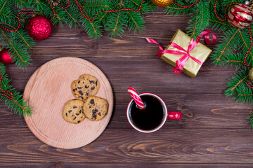 Red cup of tea with with cookies on a wooden table against the background of a Christmas tree with New Year's toys. View from above. Concept for New Year, Christmas.