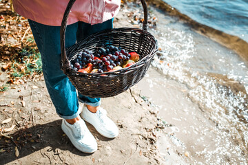 wicker basket with fruits, black grapes and apples on a background of riverside