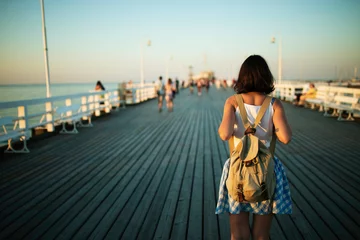 Fotobehang Young female tourist with vintage backpack walking on the wooden pier in golden hour © Woodenmen