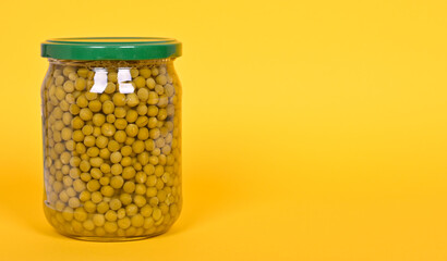 Canned green peas in a glass jar on a yellow background.