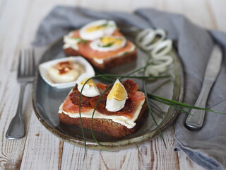 Two open sandwiches with dark rye bread with cheese, salmon fish and dried tomatoes.Healthy natural breakfast on a wooden white table.Side view.