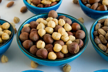 Shelled and unshelled luxury hazelnuts in a blue ceramic bowl on white surface